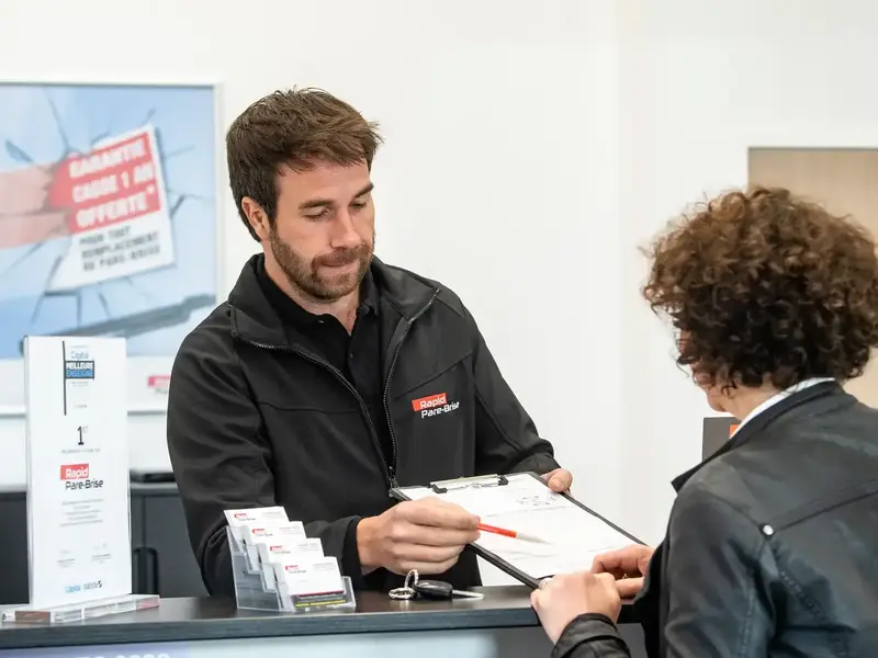 Employé Rapid Pare-Brise en train d'échanger avec une cliente au comptoir d'accueil